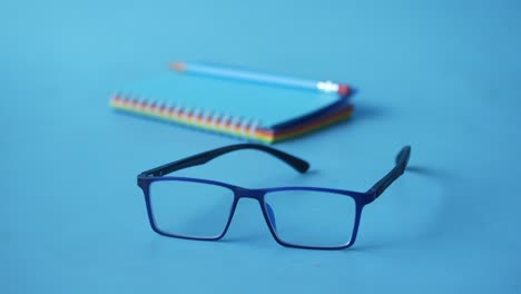 notepad, eyeglass and a pencil on blue background