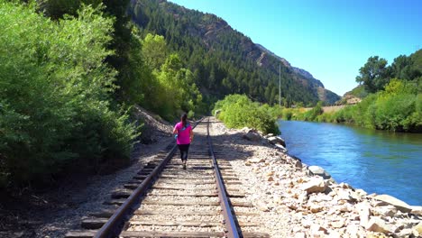 mujer de mediana edad camina sobre las vías del tren a lo largo del río en un cañón