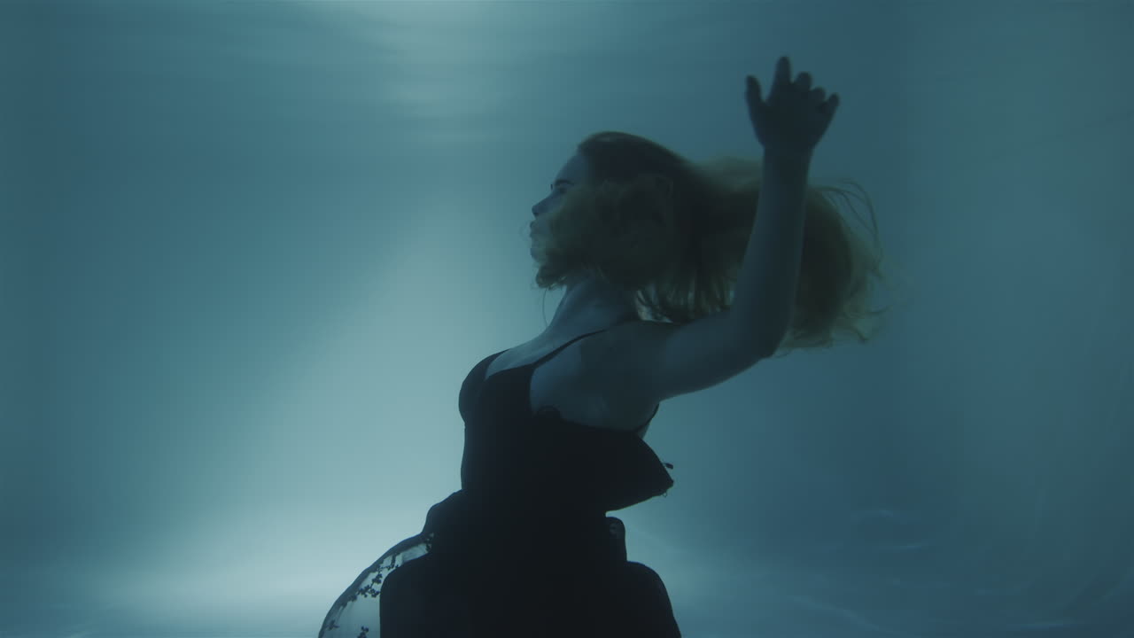 Woman with red hair posing in black dress underwater