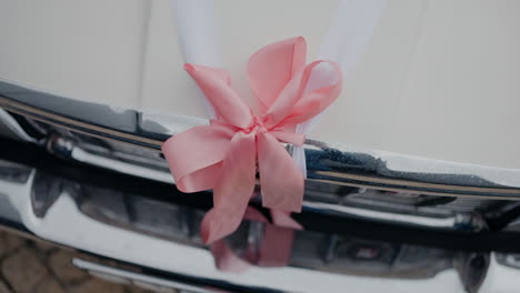 close-up of a pink ribbon bow tied on the front of a vintage car for a wedding decoration