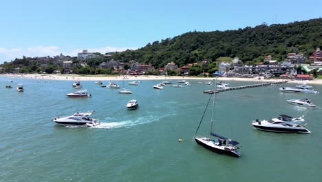 escena aérea de drones de bajo vuelo sobrevolando lanchas rápidas yates y barcos de lujo con muelle en playa paradisiaca en playa canajurê florianópolis santa catarina tropical