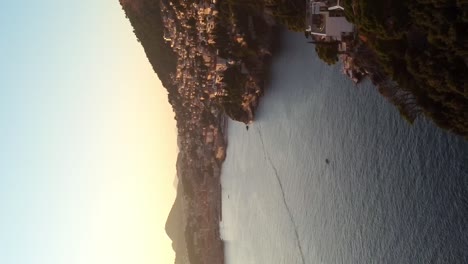 Vertical-slow-moving-backwards-drone-shot-of-Dubrovnik-coast-at-sunset