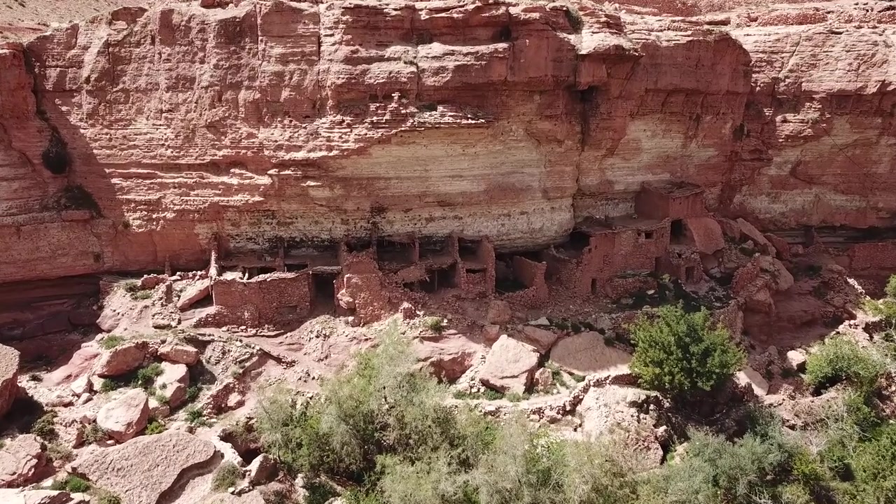 Aerial view of a desert village perched on a rocky cliff above a green oasis canyon with a winding river in Ouarzazate. Dramatic elevation and contrast ideal for cinematic and travel visuals.