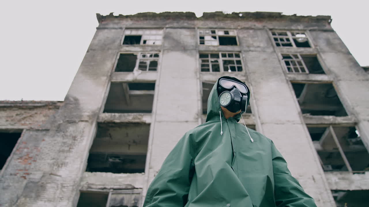 Woman in respirator and protective coat. Survivor on the background of ruined building without windows, Chemical pollution in the city. View from below.