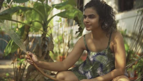 pretty indian woman with slight smile, waters garden with hose, slow motion