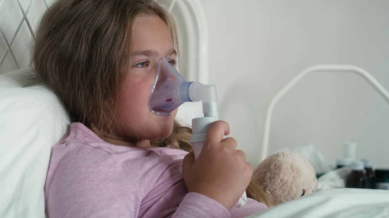 niña de edad primaria usando nebulizador en la cama en casa