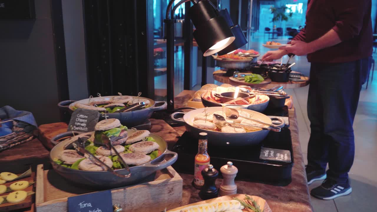 camera shot over breakfast buffet in a hotel - a man takes breakfast