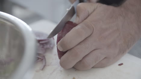 close up of a man cutting a red onion in slices on a white plate in slowmotion log