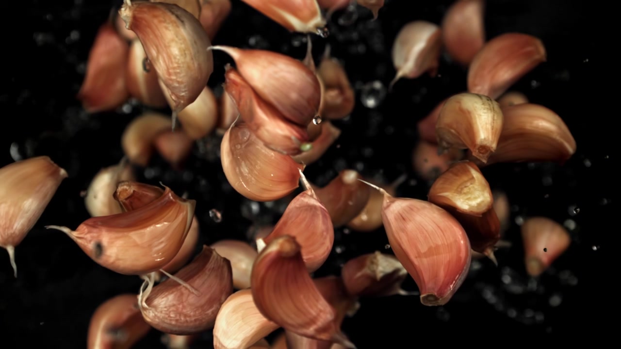 Fresh Garlic Cloves Falling with Water Droplets in Slow Motion