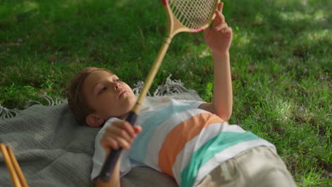 upset little boy lying blanket in park. kid examining badminton racket net