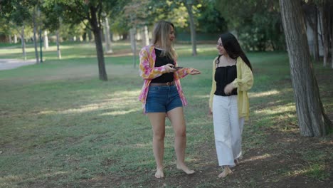 two women walking in a park, using smartphones
