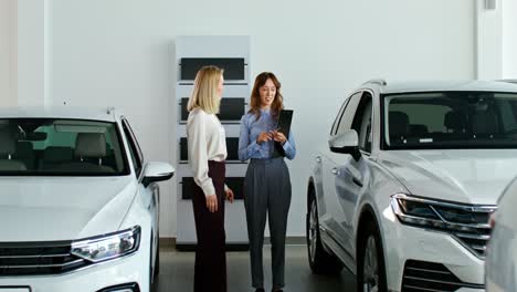 dos mujeres discutiendo coches en una sala de exposiciones