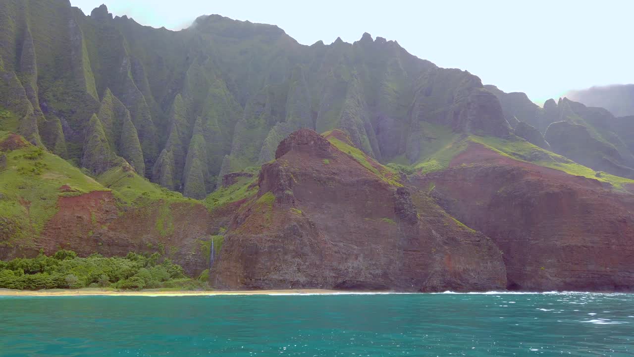 4K Hawaii Kauai, navigazione sull'oceano, panoramica da sinistra a destra da una cascata in lontananza e costa montuosa a una costa montuosa retroilluminata