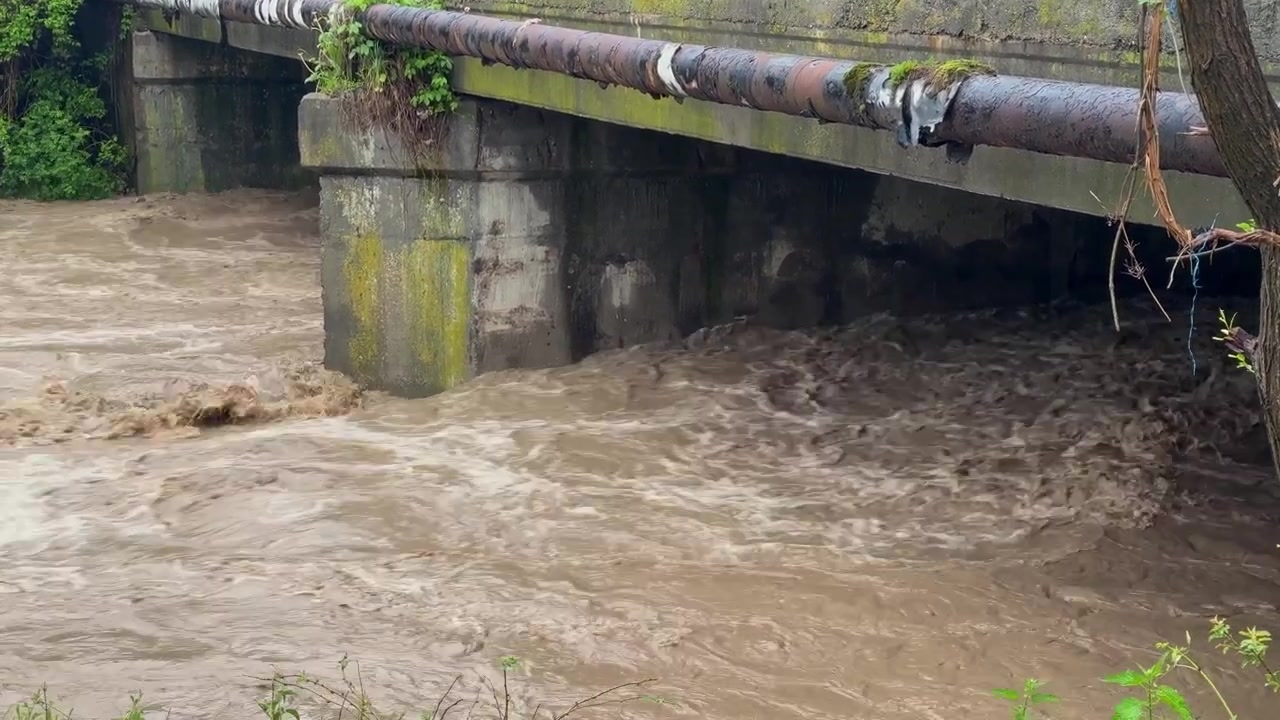 Río turbio fluyendo y creciendo rápidamente bajo un puente de hormigón. Peligrosas inundaciones causadas por el clima extremo y el cambio climático.