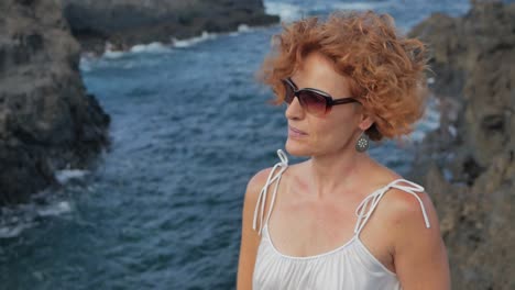 a slow motion close up shot of a redhead elegant woman with sunglasses in a cliff