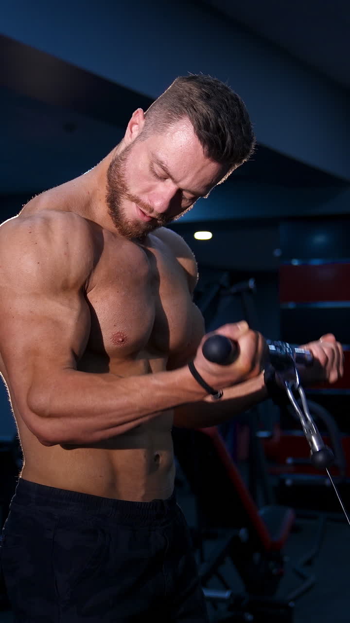 Handsome strong young bodybuilder works out on sport equipment. Strong abs. Modern gym background. Video from the side. Vertical video