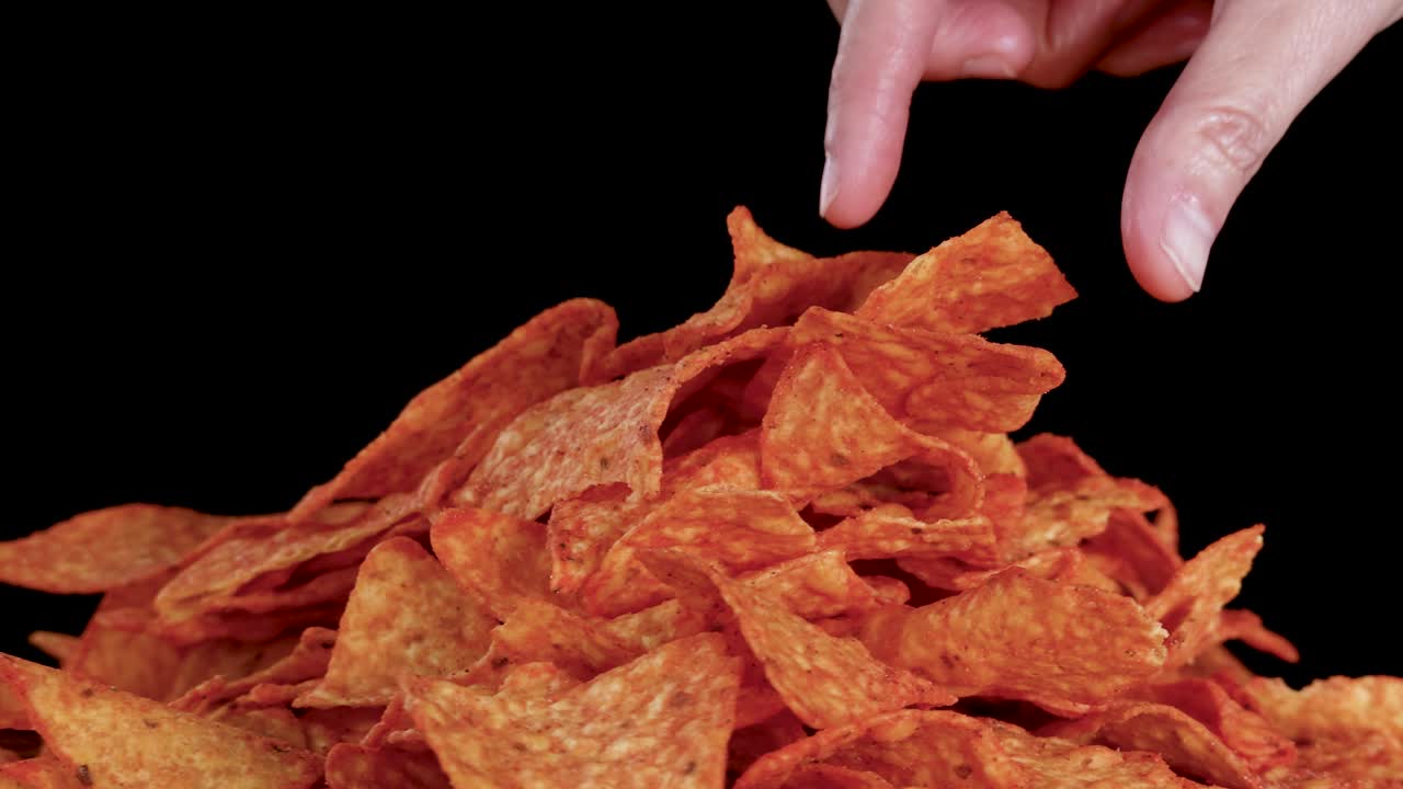 Una mano umana ruota una pila di nachos di tortilla conditi sotto una luce brillante da studio, sfondo nero