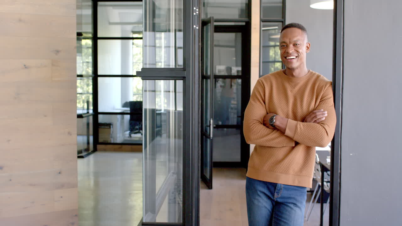 Smiling businessman standing in modern office hallway with arms crossed, copy space
