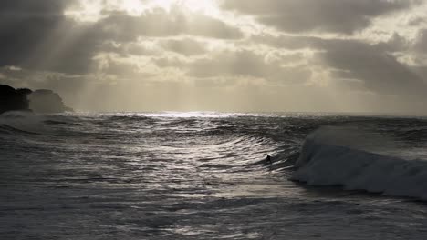 unrecognisable lone surfer riding wave from right to left of screen during stormy sunrise at bronte beach sydney
