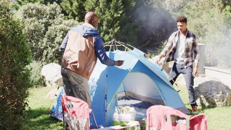 Happy-african-american-father-and-son-pitching-tent-together-in-sunny-countryside,-slow-motion