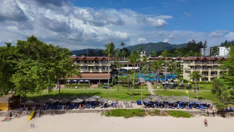 drone footage captures a luxury beach resort in phuket, thailand, showcasing vibrant pools, lush greenery, and scenic coastal views under bright daylight