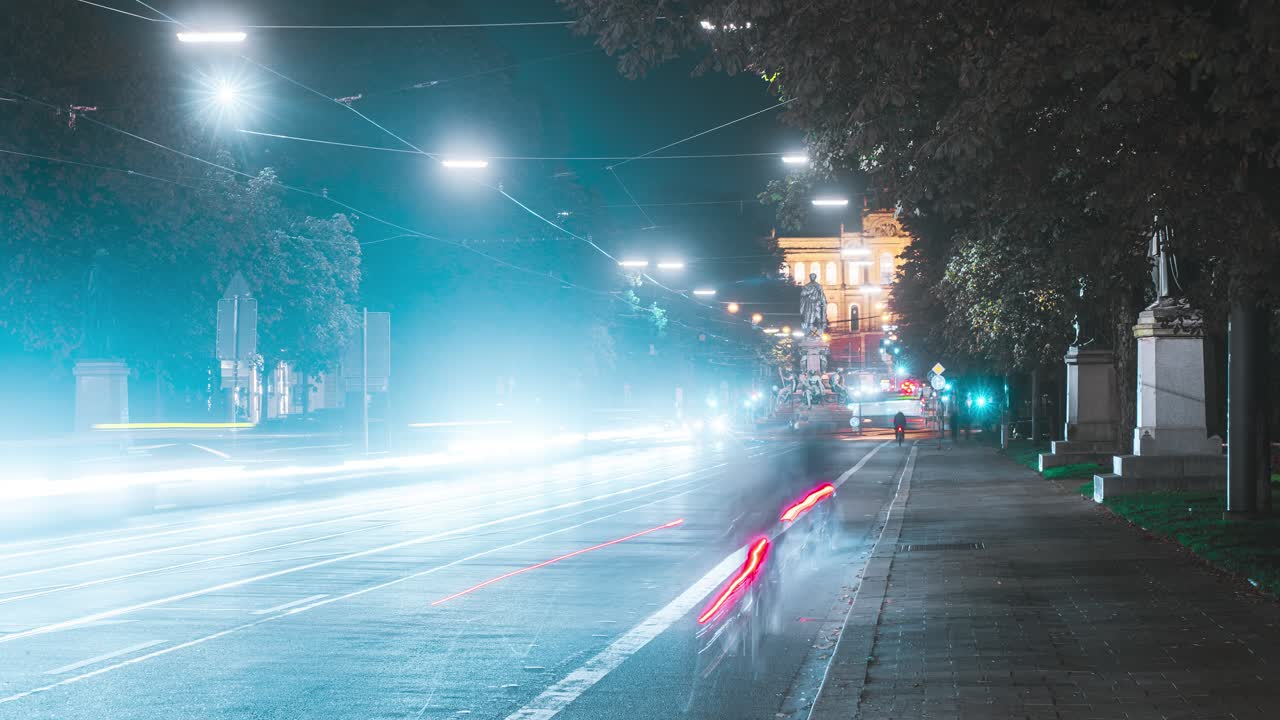 Night time lapse of road traffic in Munich. Cars and streetcars drive on street and drag light trail behind them. Busy downtown area in Germany