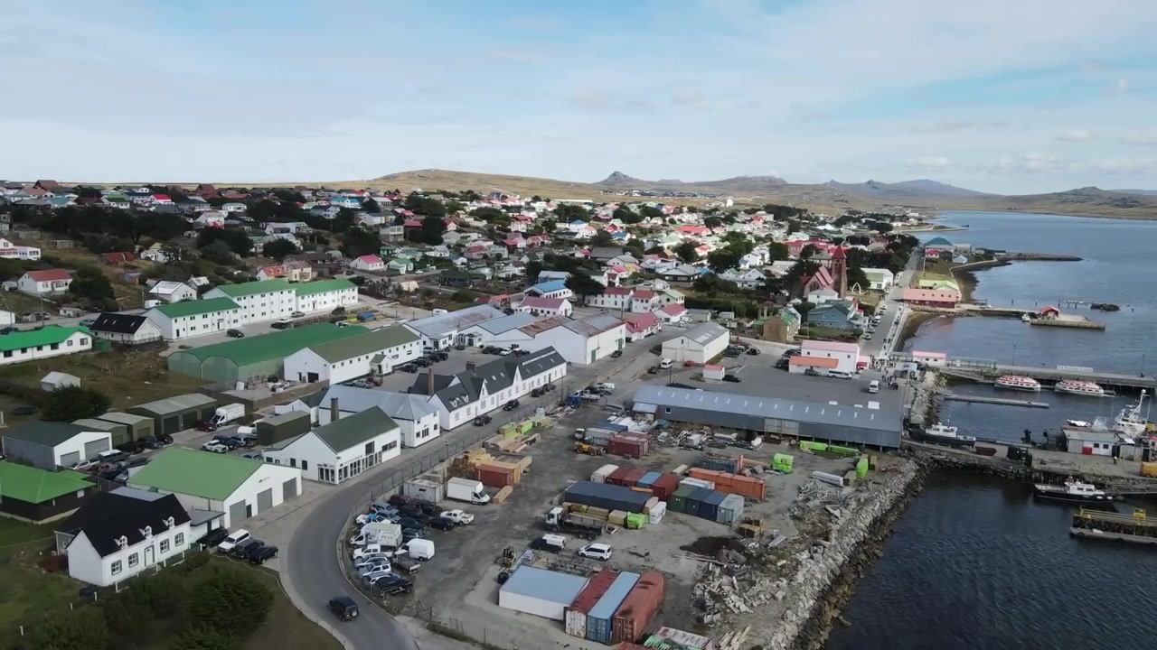 Kamera schwenkt über die lebhaften Gebäude und den geschäftigen Hafen von Stanley auf den Falklandinseln und zeigt eine lebendige Küstenszene.