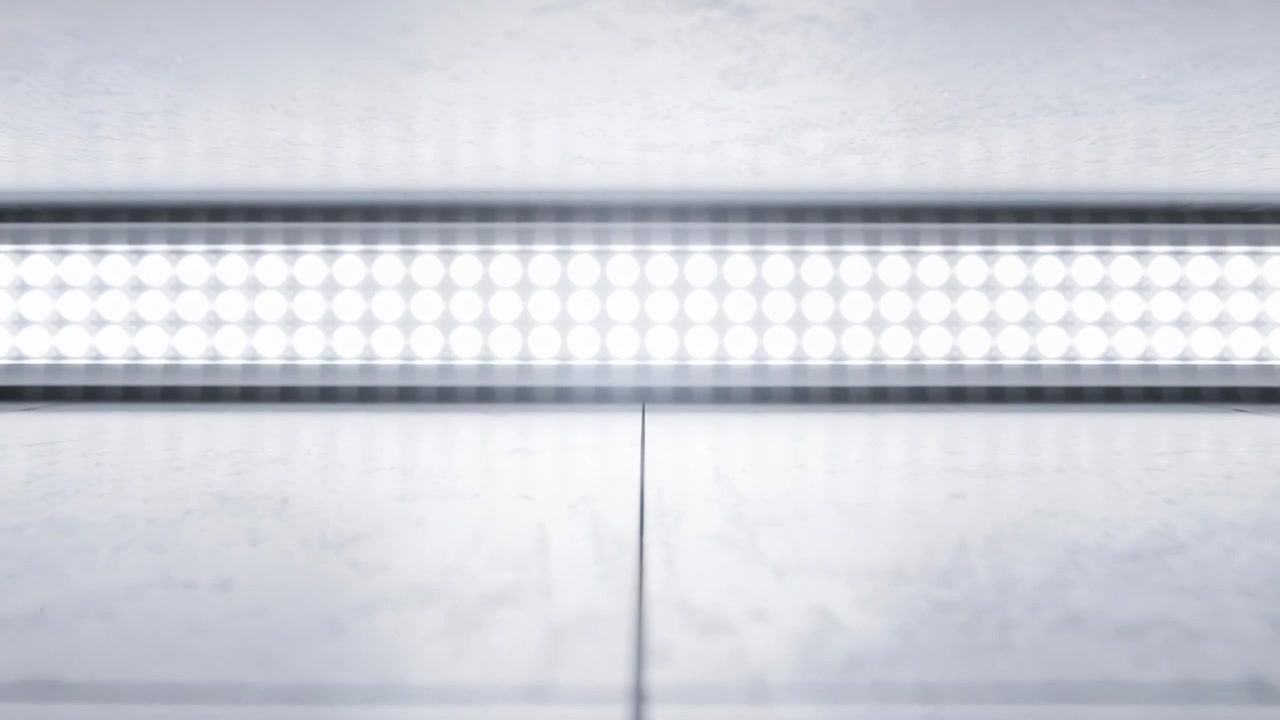Počáteční sekvence záběru, kamera se přibližuje k LED panelu v minimalistickém studiu, odhaluje šev a kabel.
