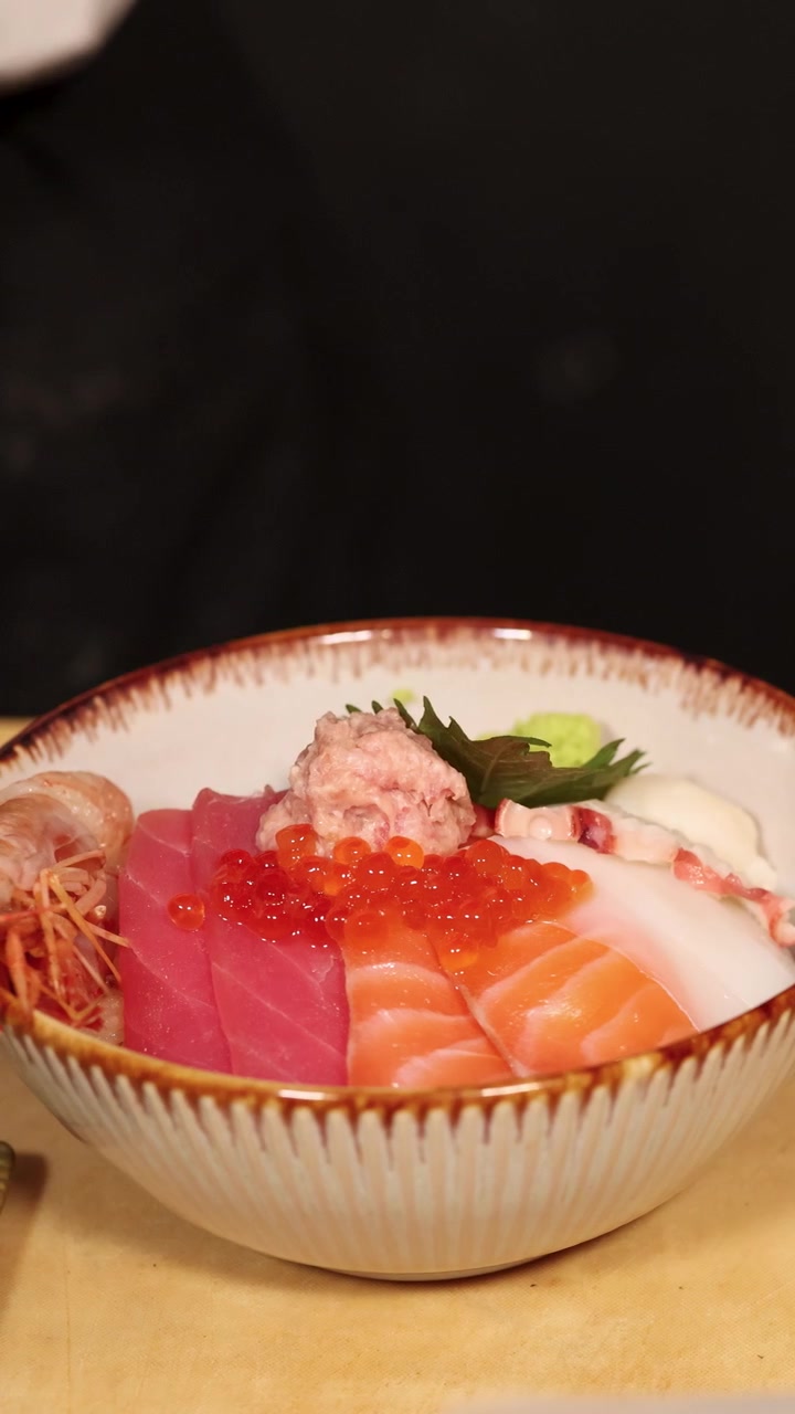 Primo piano di uno chef che usa le bacchette per guarnire una ciotola di riso fresco con frutti di mare e wasabi