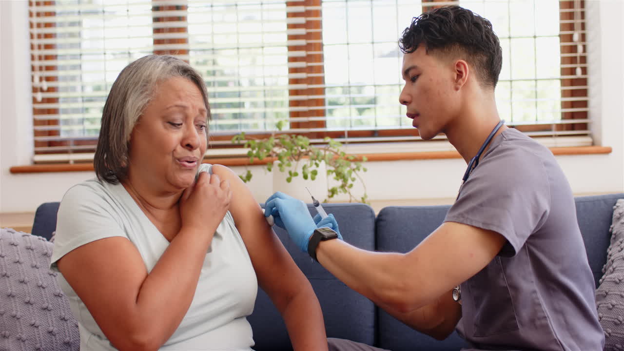 Administering vaccine, male nurse giving injection to senior woman at home
