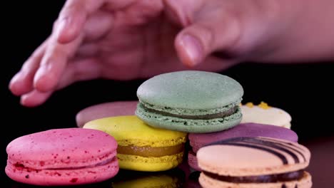 a human hand carefully arranges assorted colorful macarons on a glossy black surface under bright studio lighting, highlighting texture and vibrant dessert colors