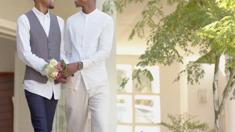 midsection of african american gay male couple holding hands and flowers at wedding, slow motion