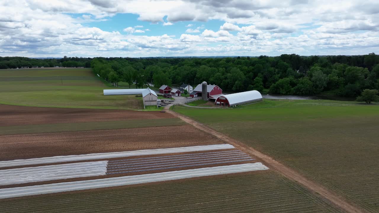Aerial approaching shot of American farmstead with modern building, silo storage and barns. Rural area of town in United States. Sunny day with cultivated fields.