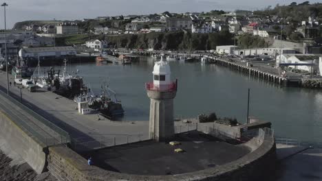 retreating aerial of lighthouse at fishing harbour in irish coast town