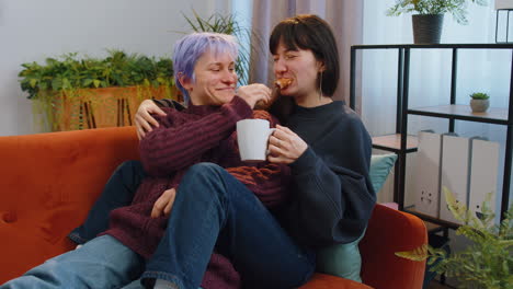 two lesbian women family couple, girl friends drinking coffee, eating croissants and talking at home