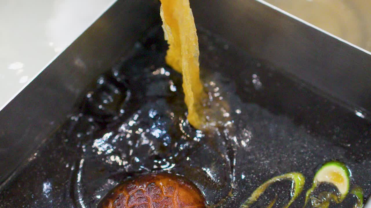 Close-up shot of chopsticks lifting tofu skin from a dark boiling sukiyaki broth with mushrooms
