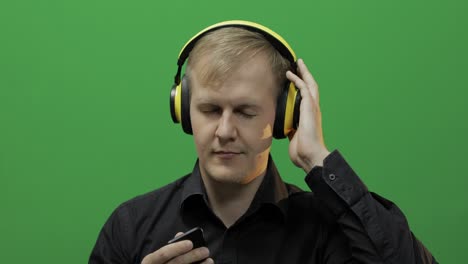 Guy-listens-to-music-in-wireless-yellow-headphones-and-dances.-Green-screen