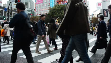 wide angle view of japanese pedestrian scramble through crowded place in the middle of shibuya square crosswalk during the rush hour with billboard and building in the background.