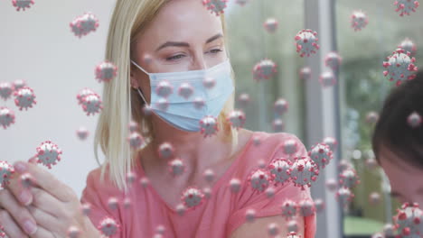 animation of covid 19 cells over caucasian blonde mother and her daughter in face masks