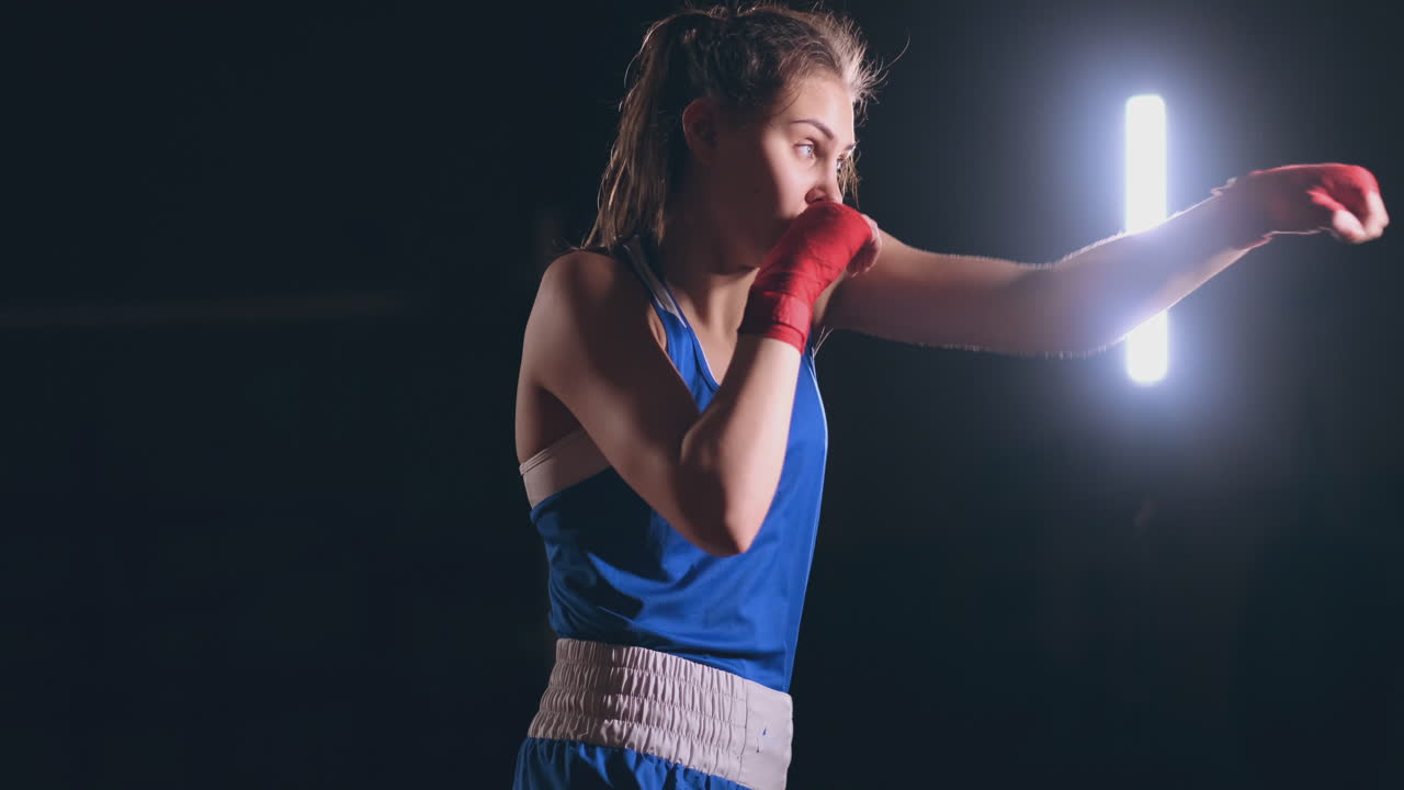 entrenamiento de boxeador femenino en una habitación oscura con luz de fondo en cámara lenta vista lateral. disparo de steadicam