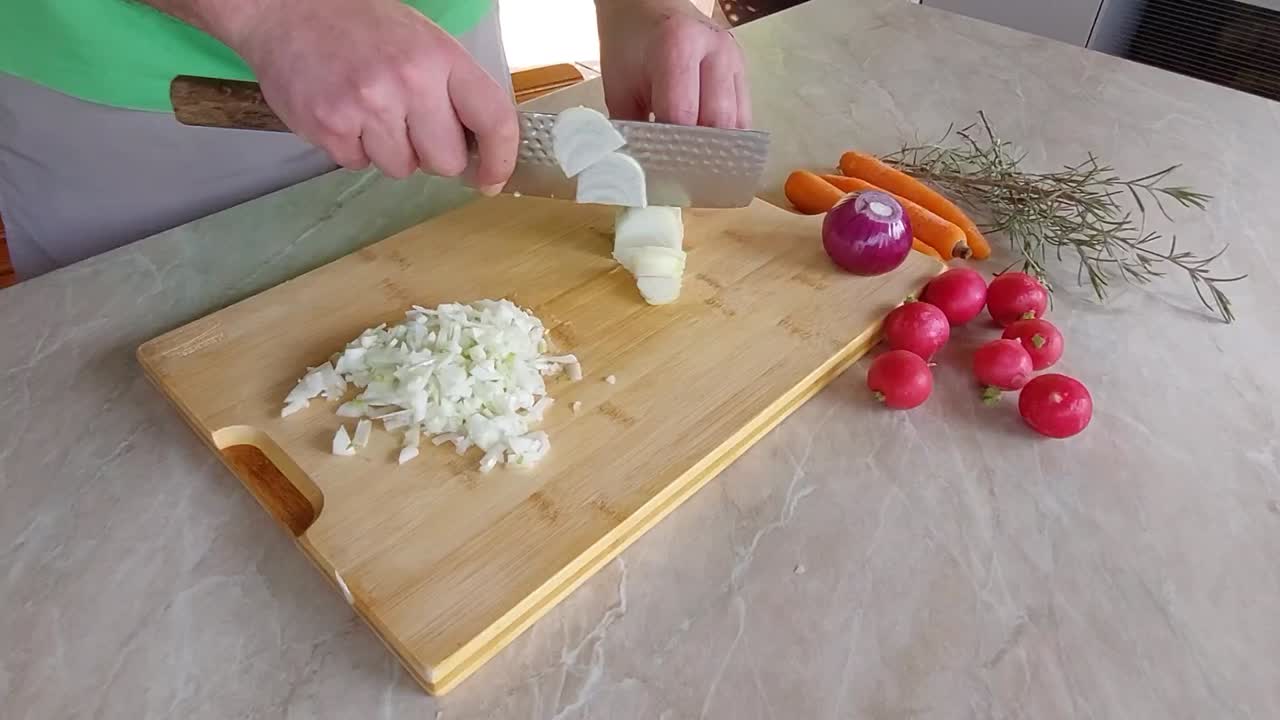 Mans hand with knife cuting red onion on wooden bamboo desk