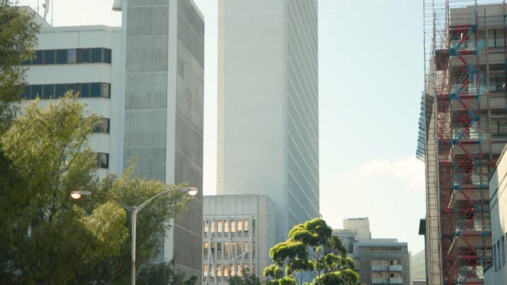Una leggera brezza si alza e il sole si sposta, muovendo gli alberi e le nuvole che fluttuano attorno a un grattacielo della città.