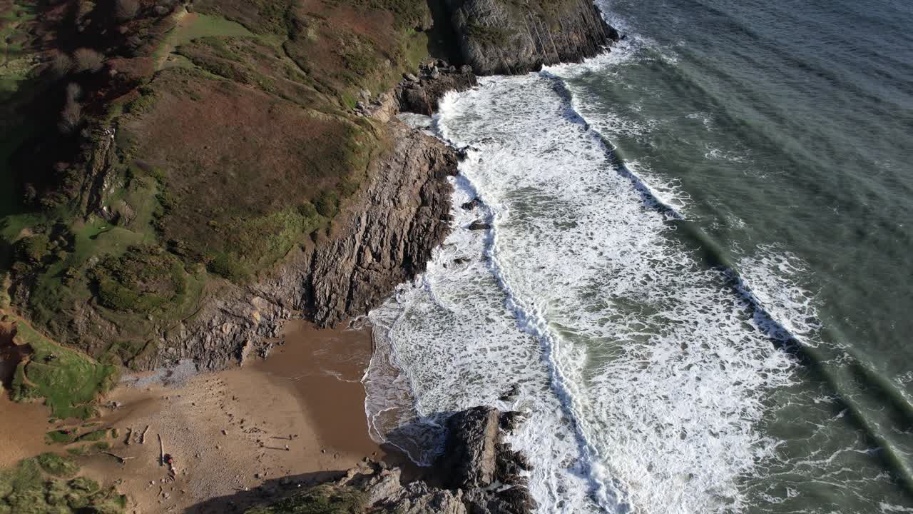 Drone circling above Pobbles Bay showing powerful dramatic rocks and rolling green cliffs on the Welsh coast