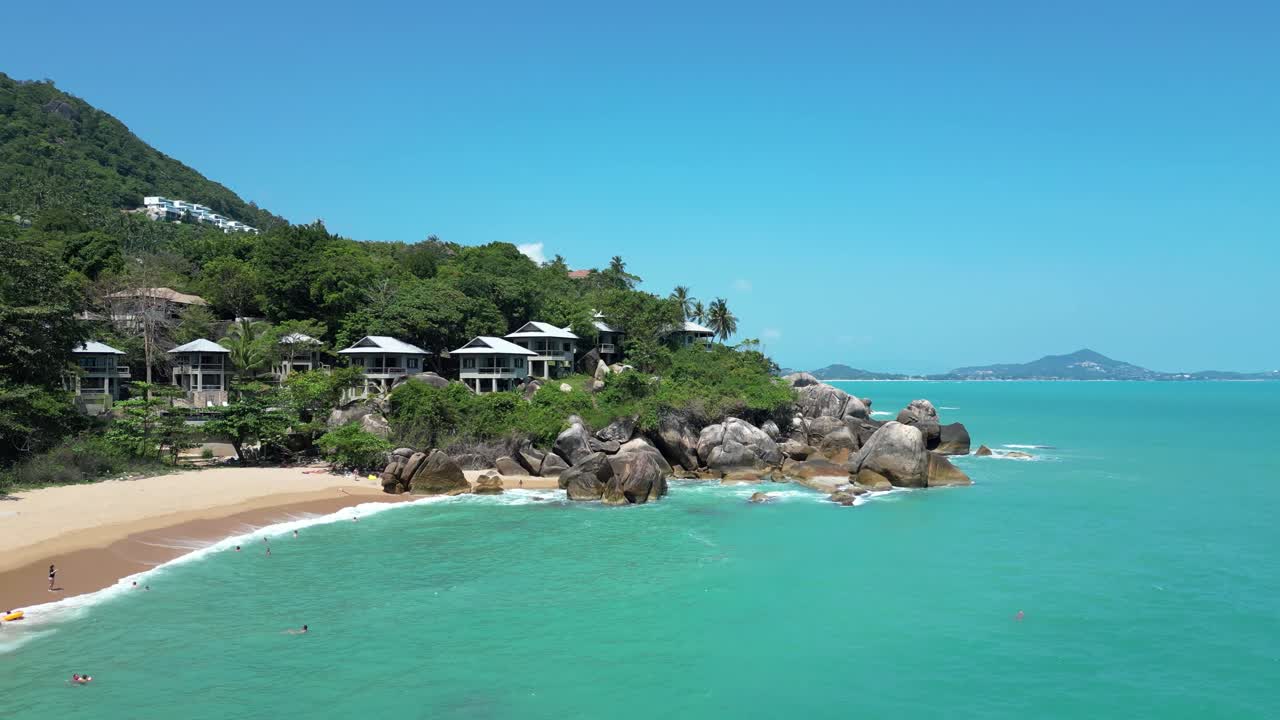 코랄 코브 해변 (koh samui) 의 무인기 영상, 푸른 물, 모래 해변, 울창한 초록색으로 둘러싸인 해변 빌라를 특징으로합니다.