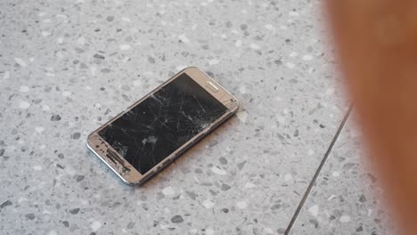 smartphone with a severely cracked and shattered screen on a speckled floor