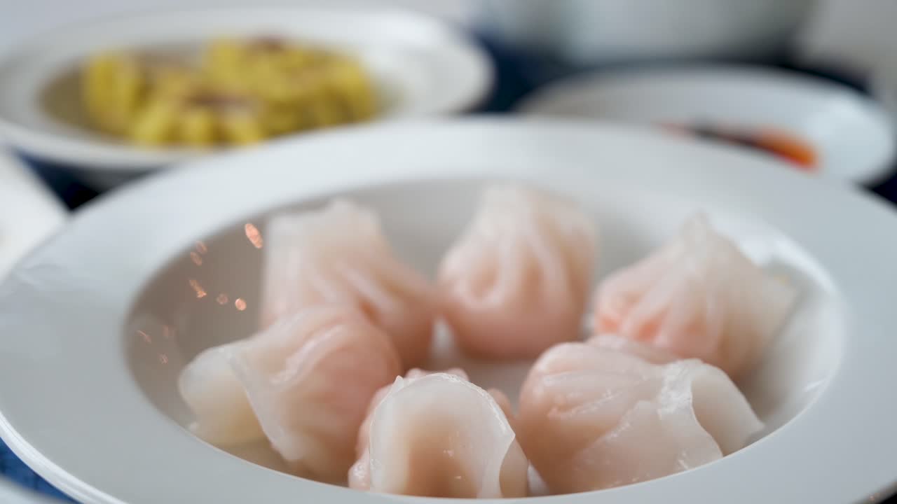 A steamed shrimp dumpling dish is seen in the foreground displayed on a table as part of a Cantonese culinary food and dim sum experience
