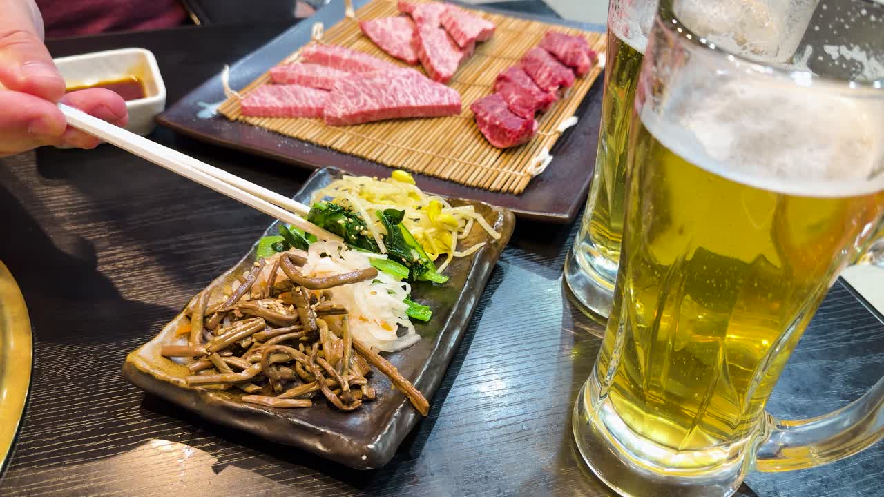 ビールジョッキの横で箸を使って味付け野菜を食べている人のクローズアップショット
