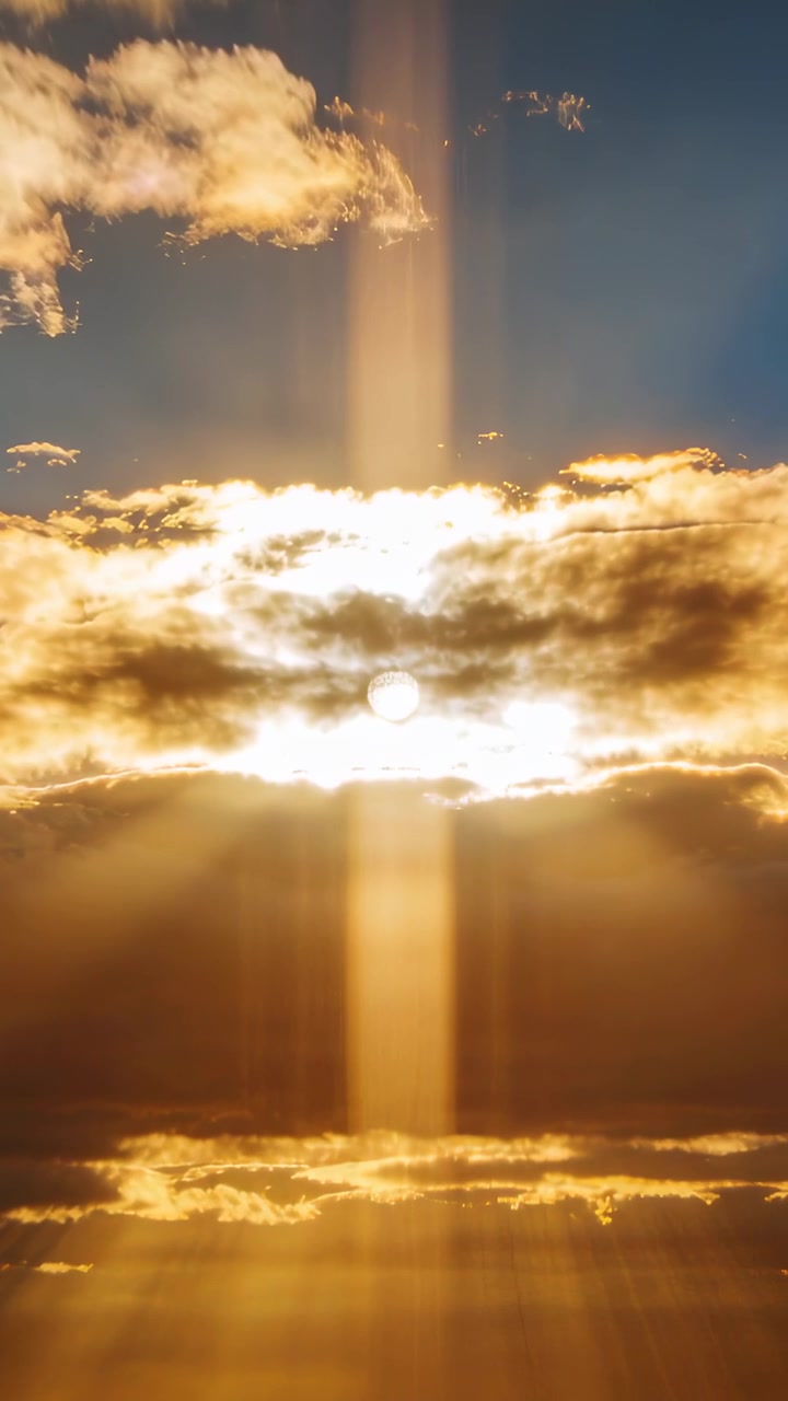 Video verticale: Bordi di nuvole che si muovono rivelando una fascia illuminata dal sole e una colonna di luce su un cielo dorato all'alba