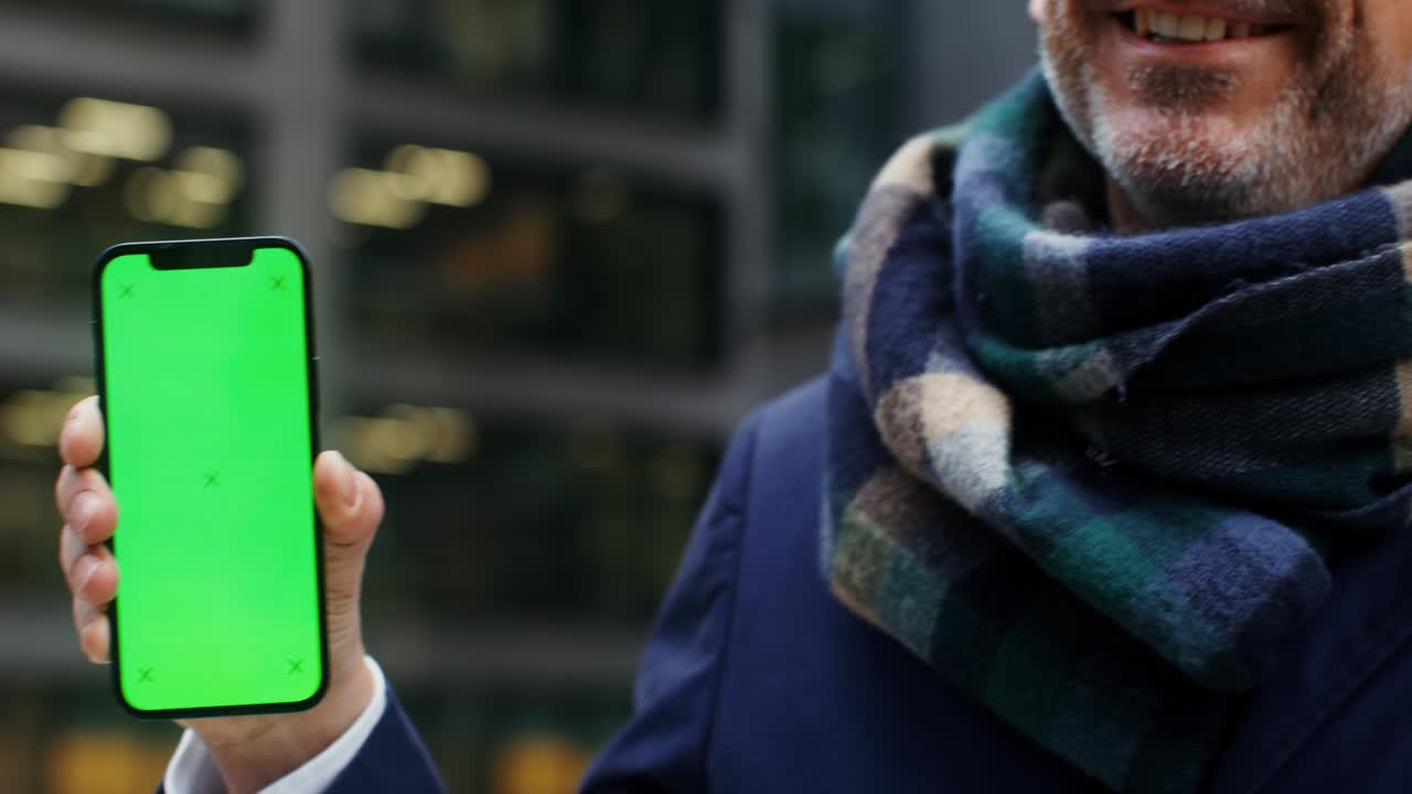 hombre sonriente en la ciudad sosteniendo un teléfono con pantalla verde