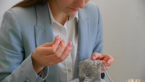 taller de costura niña sentada en la mesa en la mano coser cuentas y joyas. coser vestidos y decorar vestidos de noche con cristales.
